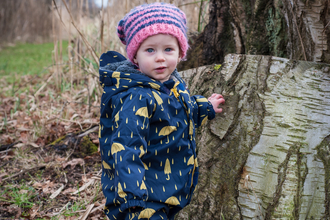 Poppy the toddler stands next to a tree stump