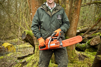 Adam stands with a chainsaw in a wood