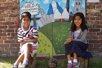 Two children sat smiling in front of Wild Stockport mural