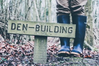 Photo of a sign reading 'Den building' next to a person in green wellies.