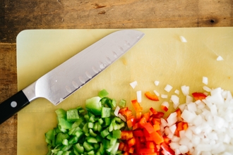 Photo of knife and chopped onion and peppers on a yellow chopping board