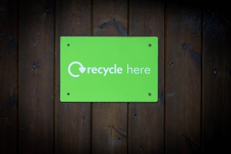 Photo of a green sign saying recycle here, on a wooden wall