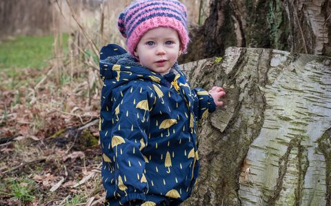 Poppy the toddler stands next to a tree stump