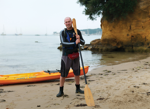 Dan stands on a beach with his kayak