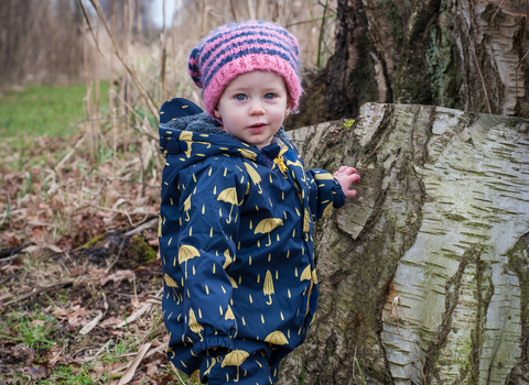 Poppy the toddler stands next to a tree stump