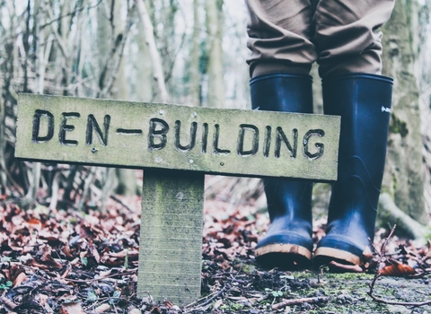 Photo of a sign reading 'Den building' next to a person in green wellies.