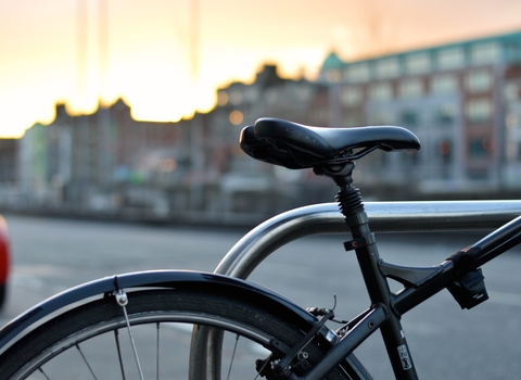 Close up photo of bike seat and wheel, with city buildings in the background