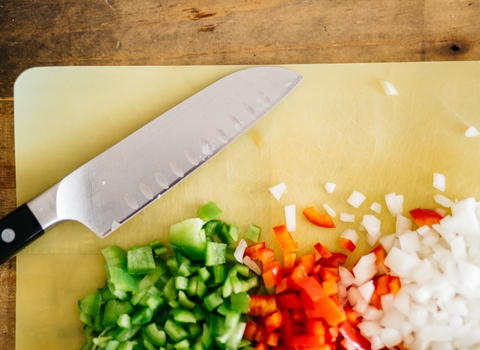 Photo of knife and chopped onion and peppers on a yellow chopping board