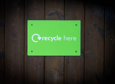 Photo of a green sign saying recycle here, on a wooden wall